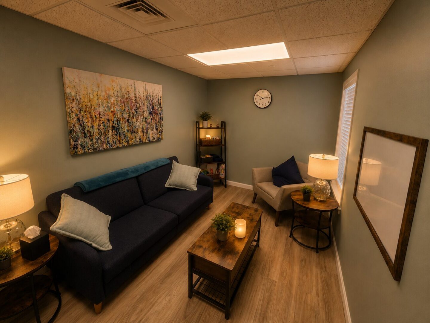 Photo of office at Sanative Counseling and Wellness Center Suite 103, room includes a couch, a chair and some shelves.